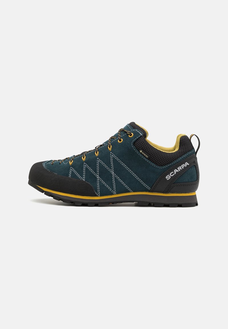 Chaussure de randonnée en suède bleu avec un capuchon en caoutchouc noir, des accents jaunes et une doublure en tissu texturé ; présente un design à lacets et une semelle robuste.