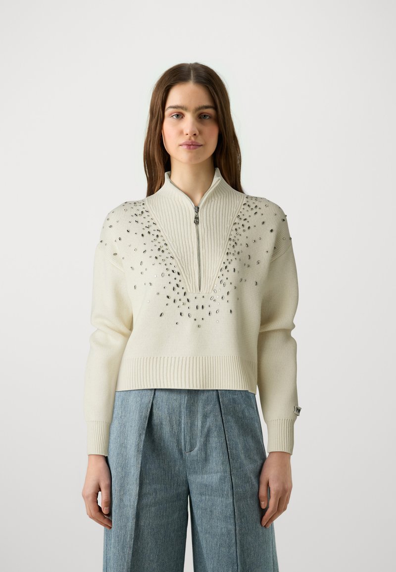 Maglione lavorato a maglia color crema con mezza zip frontale, yoke testurizzato e decorazioni di strass sparse. Bordo e polsini a costine.