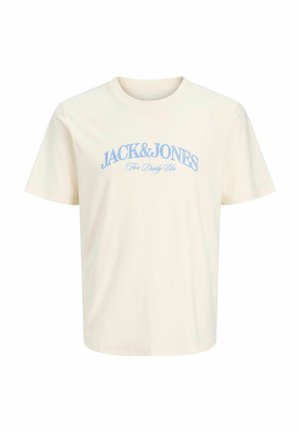 Chłopiec z kręconymi włosami, ubrany w granatową koszulę na krótki rękaw z guzikami, kremową koszulkę z grafiką, jasne dżinsowe spodenki, białe skarpetki i beżowe buty, stojący na białym tle.