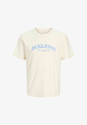 Garçon aux cheveux bouclés portant une chemise bleu marine à manches courtes boutonnée, un t-shirt crème à motif graphique, un short en jean clair, des chaussettes blanches et des chaussures beiges, debout sur un fond blanc.