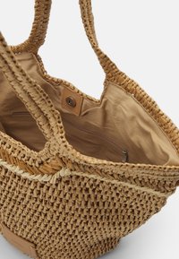 Geflochtene Strohtasche mit beigem Innenfutter. Verfügt über zwei geflochtene Griffe, einen Magnetverschluss und eine innere Reißverschlusstasche für sichere Aufbewahrung.