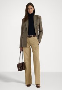 Brun rutete doblet jakke over en svart høyhalset genser, beige bukser, brun belte, og veske med kjedehåndtak. Brune hælsko.