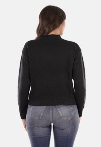 Maglione nero lavorato a maglia con collo alto, spalle scese e orlo a costine. La parte posteriore presenta un design semplice, abbinato a jeans aderenti.