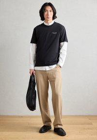 Black short-sleeve t-shirt layered over a white striped button-down, tan wide-leg trousers, and a black pleated tote. Black shoes complete the look.