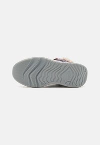 Semelle de chaussure en caoutchouc gris avec un motif de grip texturé et des accents en relief. L'intérieur présente un revêtement doux et des détails en tissu coloré sur le dessus.
