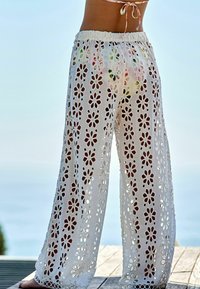 Witte, haakstijl broeken met bloemen uitsparingen. Elastische tailleband, ruime pasvorm, lichtgewicht stof, geschikt voor warm weer.