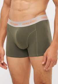 Olivgrüne Boxer Shorts mit einem grauen Bund, der "JACK & JONES" in Orange zeigt. Weicher Stoff, taillierte Passform und kontrastierende Nähte.
