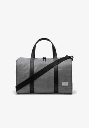 Sac de voyage en tissu gris avec des accents et des poignées en cuir noir. Il dispose d'un dessus zippé et d'une bandoulière réglable.