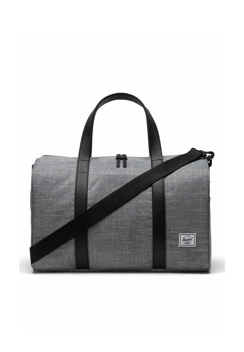Sac de voyage en tissu gris avec des accents et des poignées en cuir noir. Il dispose d'un dessus zippé et d'une bandoulière réglable.