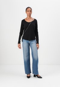 Svart langermet skjorte, lyseblå vide jeans og svarte spisse sko. Modellen bærer en sølvfarget crossover bag.