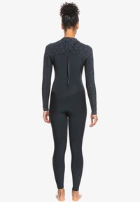 Neopreno negro de cuerpo entero con paneles de hombros texturizados, mangas largas y cremallera trasera. Material suave y elástico.