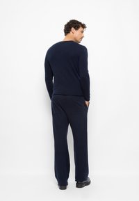 Marineblauer gestrickter Pullover mit langen Ärmeln, kombiniert mit passenden Hosen. Das Outfit zeichnet sich durch eine lockere Passform und eine weiche Textur aus.