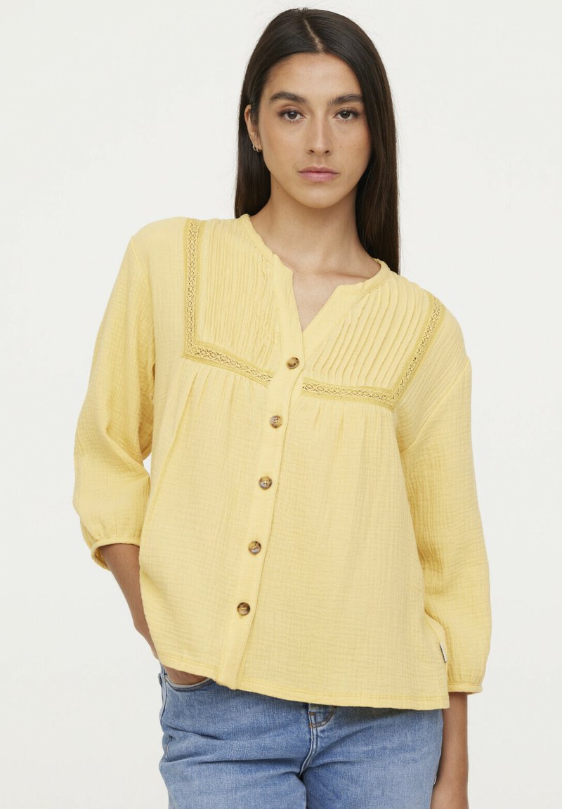 Blouse jaune à boutons avec un design texturé et plissé, ornée de dentelle, présentant des manches trois-quarts et une coupe décontractée.
