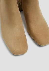 Bottines en suède beige avec un bout carré, texture lisse et un talon épais. Pas de matériel ou d'ornements visibles.