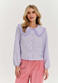 Jasnofioletowa bluzka w kratkę z falbaniastym kołnierzykiem, z przodem na guziki i kwiecistą naszywką. Długie rękawy i strukturalny materiał; luźny krój.
