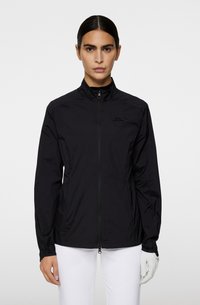 Zwarte lichte windbreaker jas met hoge kraag, voorrits en minimalistisch logo detail op de borst. Glad textuur, nauwsluitend ontwerp.
