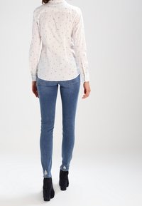 Hvid langærmet skjorte med et subtilt print, parret med lyseblå skinny jeans og sorte højhælede ankelstøvler.