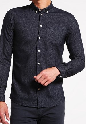 Camicia a maniche lunghe grigia scura con bottone in un tessuto testurizzato. Presenta una tasca sul petto, colletto con bottoni e bottoni bianchi.