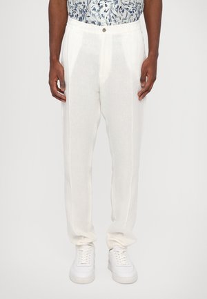 Pantalons en lin blancs avec une coupe décontractée, dotés d'une fermeture à bouton, de poches latérales et d'une texture lisse et légère. Portés avec des baskets blanches.