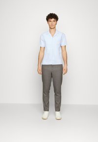 Light blue short-sleeve shirt with a collar, button front, and textured fabric, paired with gray tailored pants and white sneakers.