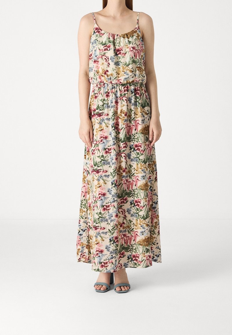 Robe maxi fleurie à fines bretelles, dotée d'une taille cintrée et d'un imprimé floral multicolore sur un fond clair. Portée avec des talons bleus.