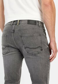 Gray denim jeans featuring a slim fit design, five pockets, visible stitching, and a black label at the waistband.