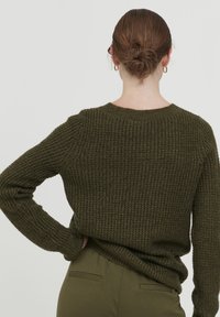 Olijfgroen gebreid trui met ribbeltextuur, ronde halslijn en lange mouwen. Achteraanzicht toont iets laten vallen schouders en een relaxte pasvorm.
