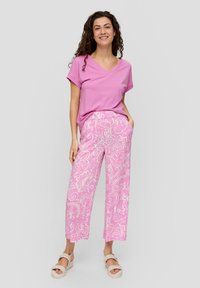 Roze v-hals t-shirt gecombineerd met lichtroze gestreepte broek met brede pijpen en bloemdesigns. Het model draagt neutraalgekleurde slidesandalen.