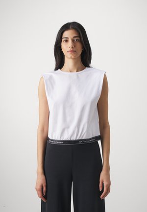 Top corto senza maniche bianco con scollatura rotonda e dettaglio del logo. Abbinato a pantaloni neri a vita alta con elastico brandizzato.