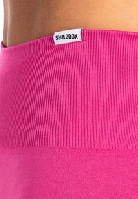 Roze geribbelde sportleggings met een gladde textuur, voorzien van een wit merkelabel bij de tailleband voor identificatie.