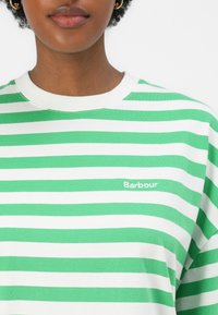 Zeleno-bílý pruhovaný tričko s kulatým výstřihem vyrobené z měkké tkaniny; na levé straně má malé logo "Barbour".