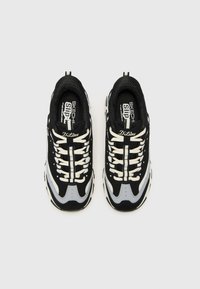Black and grey athletic sneakers feature a mesh upper, textured fabric, thick white laces, and a chunky sole with contrasting accents.