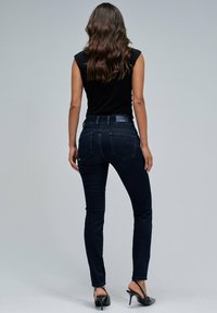 Jeans skinny de mezclilla azul oscuro con cintura media, que cuentan con bolsillos traseros y costuras en contraste, combinados con una blusa sin mangas negra.