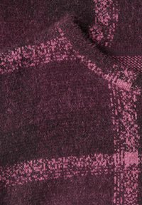 Gros plan d’un tissu doux et duveteux de couleur violet foncé avec des motifs géométriques et rayures roses, montrant la texture et les détails du tricot.