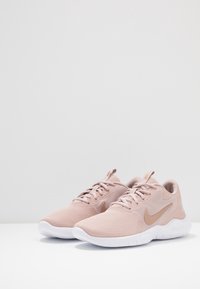 Baskets de sport rose clair avec un dessus en mesh respirant, des accents texturés et des semelles en caoutchouc blanches. Comprend un logo sur le côté et des lacets ronds.