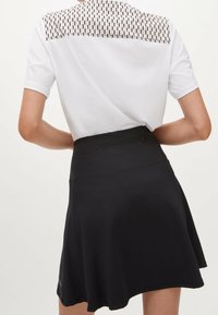 Svart skort med en utsvängd design, med en texturerad vit och mönstrad halsringning. Inkluderar en zipficka på baksidan för funktionalitet.