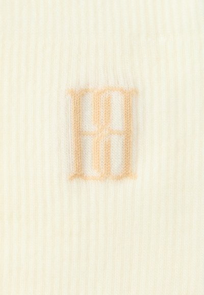 Kapa v smetanasti barvi z mehkimi rebrastimi teksturami in nežnim breskvinim vezenjem inicialk "HH" na sprednji strani.