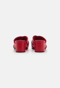 Mules rouges à talons avec une finition laquée lisse, dos incurvé et épais talon bloc. Design ouvert à l'avant et sur les côtés sans embellissements visibles.