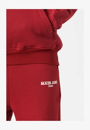 Czerwone dresy wykonane z polaru z ściągaczem w pasie. Na dolnej części lewego nogawki widnieje napis "SIXTH JUNE PARIS" w białym kolorze.