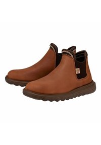 Botas de tobillo de cuero marrón con paneles laterales elásticos, suelas marrones texturizadas y una punta redondeada. Presentan un parche de logo en el lado.