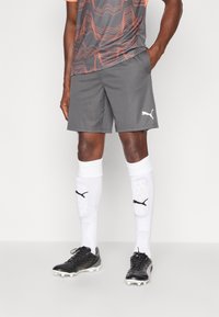 Grå sportskort, oransje mønstrete treningsskjorte, hvite sokker med sorte detaljer, og svarte fotballsko med hvite knotter.