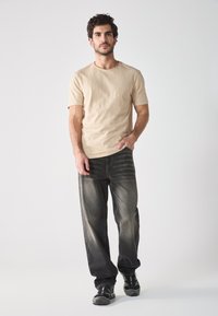 Beige t-paita lyhyillä hihoilla yhdistetty tummiin farkkuihin. T-paidoissa on tekstuuri pinta; farkuissa on haalistunut design. Mallilla on päällään mustat urheilukengät.