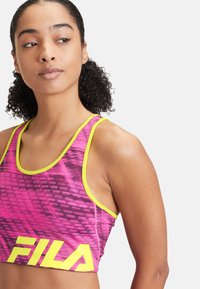 FILA idrottsbh i livlig rosa med ett geometriskt mönster, med gula detaljer och en logotyp. Materialet är stretchigt och åtsittande.