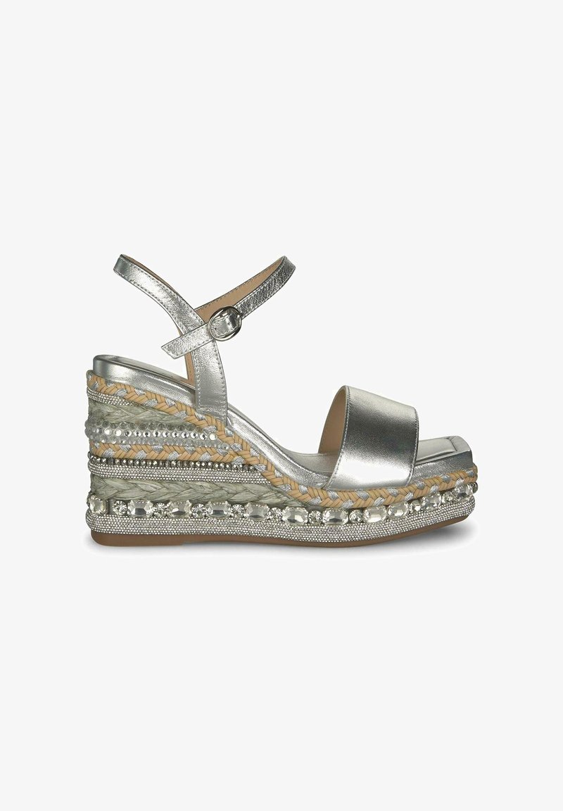 Zilverkleurige metallic wedge sandalen hebben een brede voorband, een verstelbare enkelband en een gelaagde, gestructureerde middenzool met decoratieve accenten.