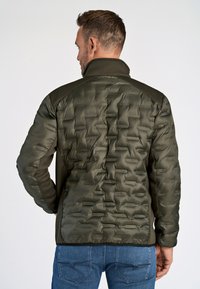 Vadderad olivgrön jacka med en texturerad yta, hög krage och nätpaneler på sidorna; har dragkedjestängning och texturerade detaljer.