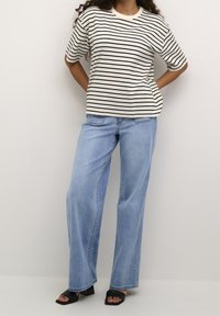 Camiseta de rayas en crema y negro, combinada con unos vaqueros de pierna ancha en azul claro. La camiseta tiene mangas cortas y un cuello redondo. Sandalias de tacón negras.