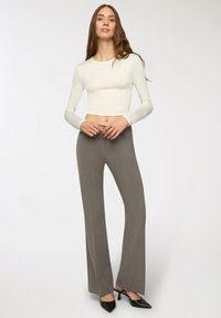 Top bianco a maniche lunghe cropped abbinato a pantaloni grigi a gamba larga. I pantaloni presentano un sottile motivo a righe verticali e tacchi neri eleganti.