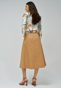 Blusa floral crema con mangas largas, combinada con una falda midi de color camel. La modelo lleva sandalias de tiras en tono beige. Texturas suaves y corte relajado.