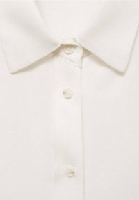 Witte polo met een textuurstof, een klassieke kraag en vijf knopen aan de voorkant met een gladde afwerking.