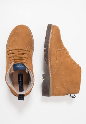 Bottes basses en daim marron avec surface texturée, design à lacets, coutures blanches contrastantes et semelles en caoutchouc présentant un motif tacheté.